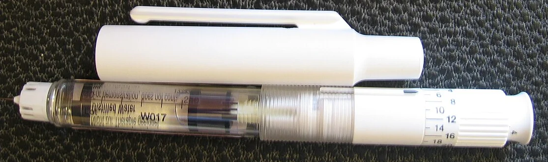 Weißer Insulin-Fertigpen mit abgenommener Kappe auf dunkler Unterlage; am Ende die Dosierskala mit Einstellrad.