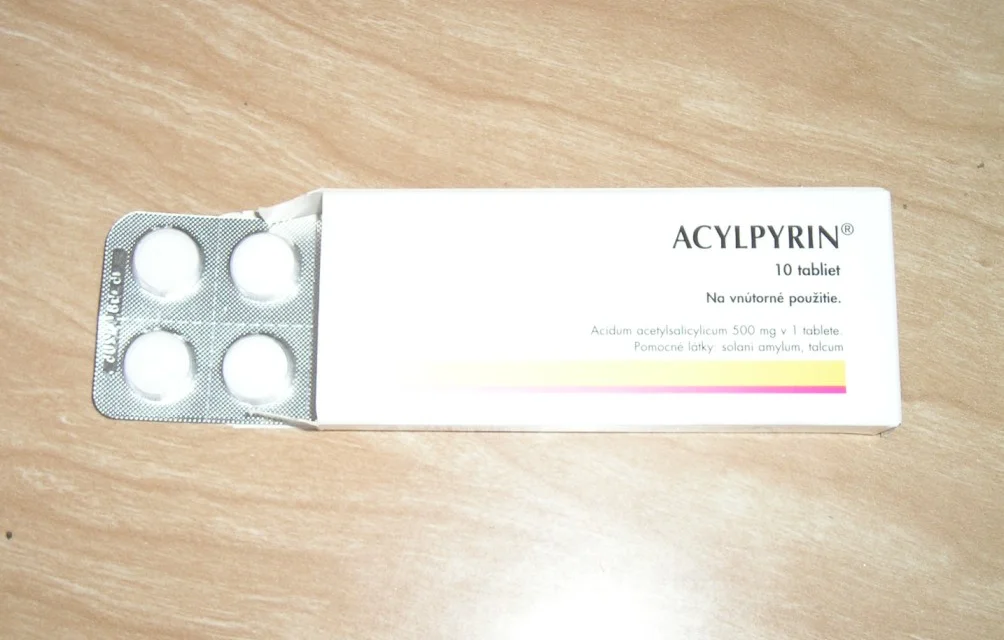 Geöffnete Faltschachtel mit Blister und vier weißen Tabletten; auf der Packung steht „Acidum acetylsalicylicum 500 mg“.