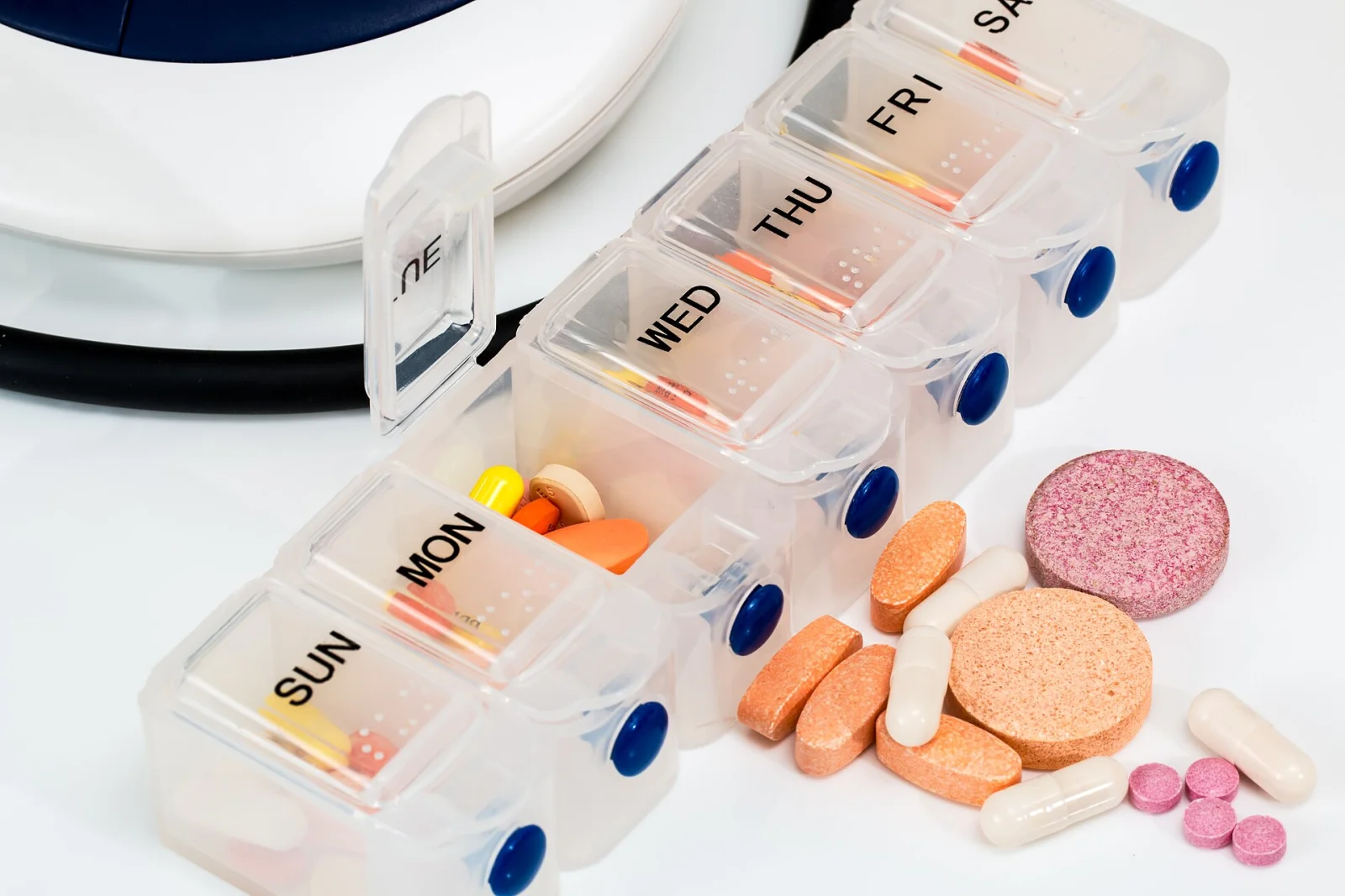 Wochendosierer mit Tabletten und Kapseln neben einem Blutdruckmessgerät