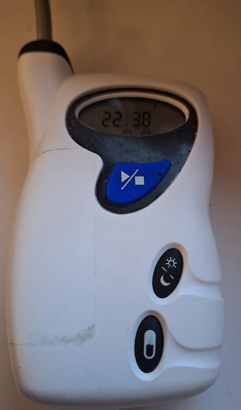 Tragbares Aufzeichnungsgerät der 24-Stunden-Blutdruckmessung mit Schlauchanschluss oben, Uhrzeitanzeige, blauer Start-Stopp-Taste und einer Taste mit Sonnen- und Mondsymbol.