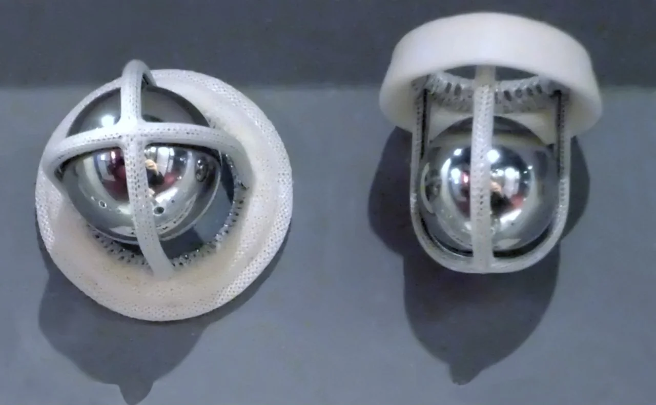 Zwei ältere Herzklappenprothesen mit glänzender Stahlkugel in einem Käfig aus stoffbezogenen Bügeln über einem weißen Nahtring, links von oben, rechts von der Seite gesehen