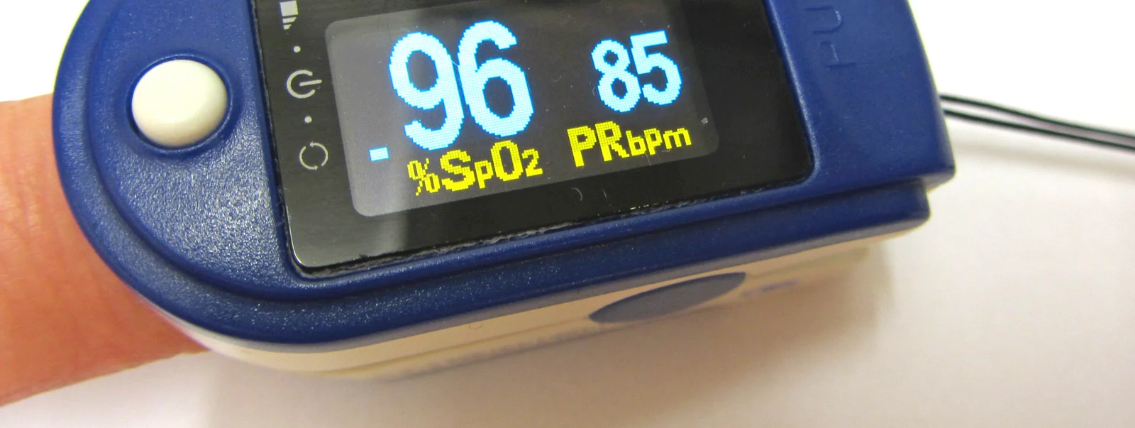 Fingerclip-Pulsoxymeter an einer Fingerkuppe; das Display zeigt links SpO₂ 96 Prozent und rechts eine Pulsfrequenz von 85 pro Minute.