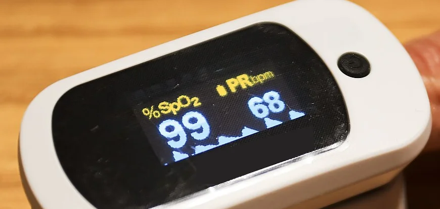 Fingerpulsoxymeter in Nahaufnahme; die Anzeige zeigt SpO₂ 99 %, eine Pulsfrequenz von 68 pro Minute und eine gleichmäßige, gut ausgeprägte Pulskurve.