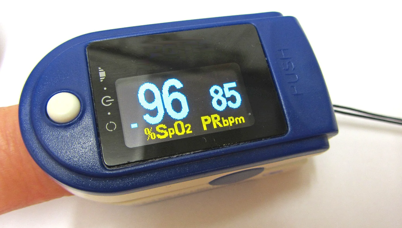 Fingerpulsoxymeter am Zeigefinger; die Anzeige zeigt SpO₂ 96 % und eine Pulsfrequenz von 85 pro Minute.