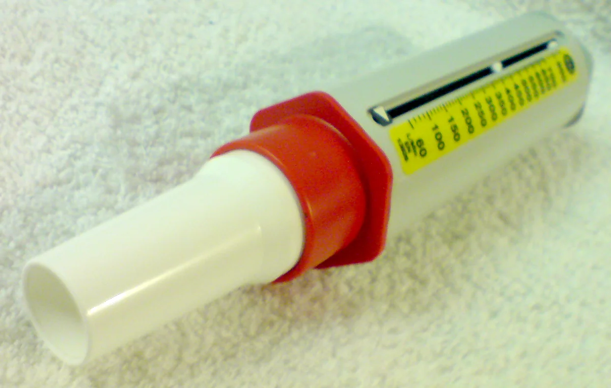 Mechanisches Peak-Flow-Meter: weißes Mundstück, rote Manschette und durchsichtiges Gehäuse mit Schiebezeiger über einer gelben Skala in Liter pro Minute, beginnend bei 60.