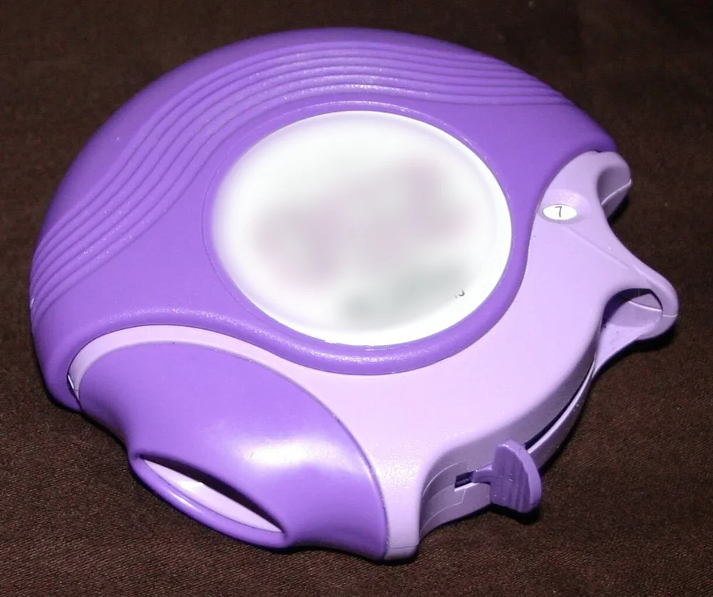 Runder violetter Pulverinhalator vom Diskus-Typ mit unkenntlich gemachtem Etikett, seitlicher Öffnung und kleinem Zählfenster, das die Zahl 7 zeigt.