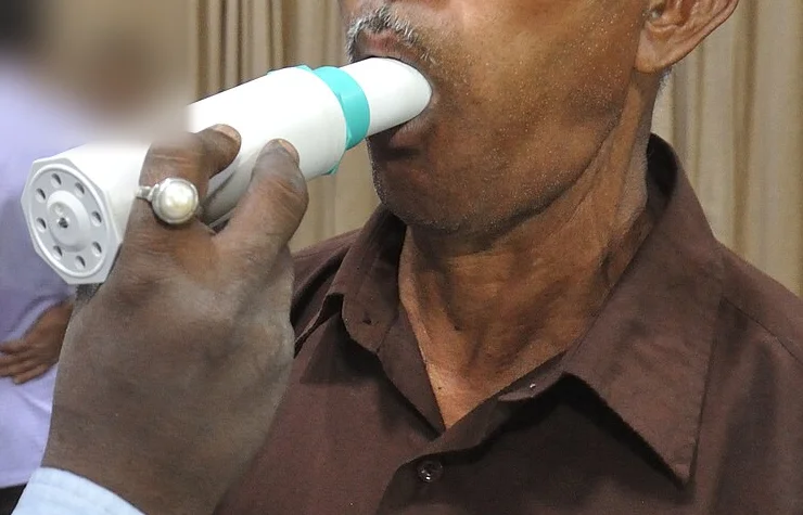Ausschnitt ohne Gesichter: Die Lippen eines Patienten umschließen das Mundstück eines Handspirometers dicht; die Hand der untersuchenden Person hält das Gerät.