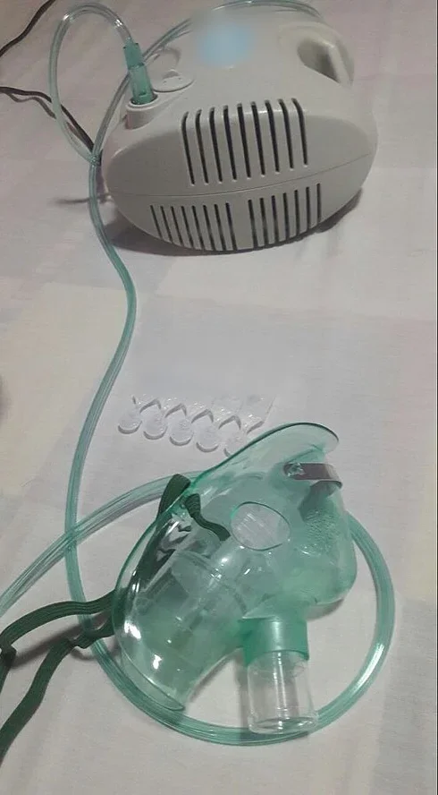 Druckluftvernebler: Kompressor mit Luftschlauch zur Verneblerkammer an einer Gesichtsmaske, daneben Einzeldosis-Ampullen mit Inhalationslösung.