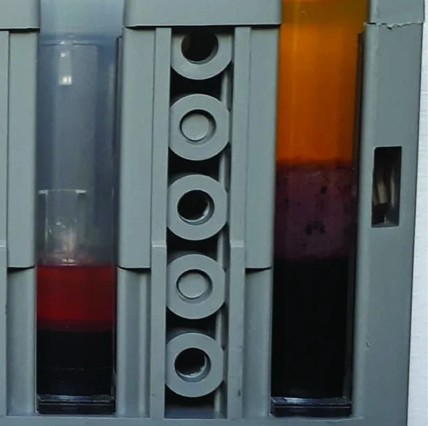 Zwei zentrifugierte Heparinproben nebeneinander in einem Ständer: links eine Blutgasprobe mit rötlichem, hämolytischem Plasma über den Blutzellen, rechts ein Lithium-Heparin-Röhrchen mit klarem, gelbem Plasma.