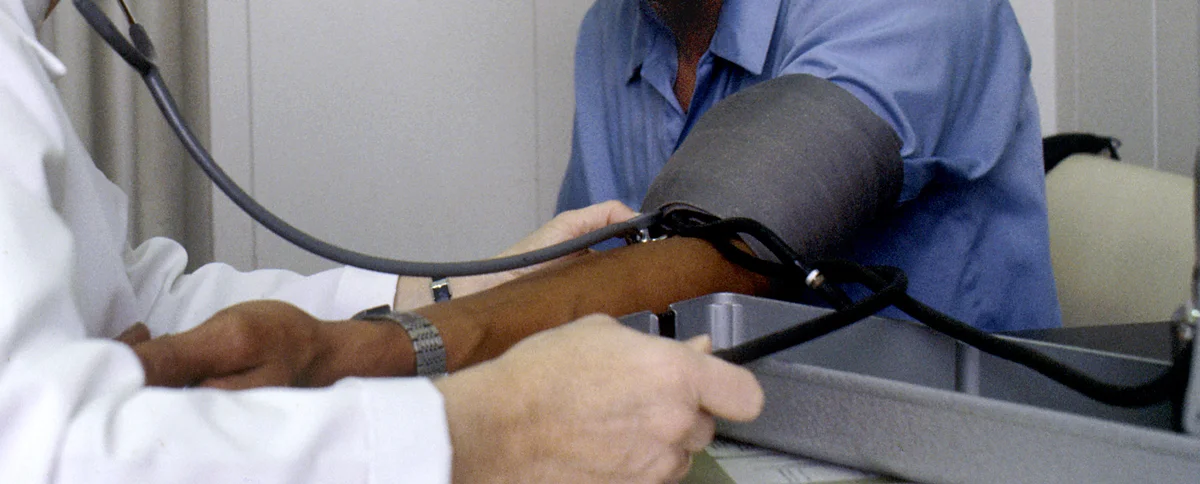 Ausschnitt einer Praxismessung: Oberarmmanschette am sitzenden Patienten, der Unterarm liegt gestützt auf dem Tisch, das Stethoskop liegt in der Ellenbeuge über der Arteria brachialis.